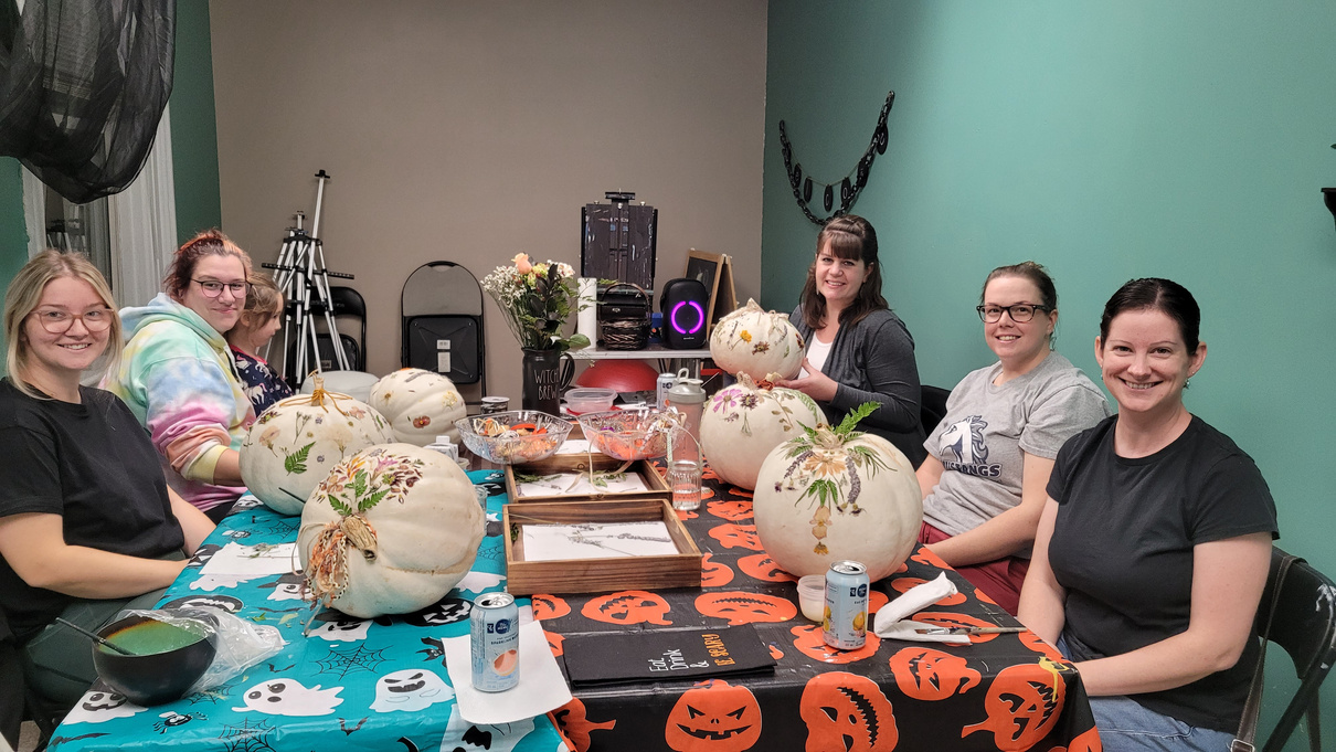 a group of individuals sitting around a table with pumpkins on it for a craft workshop